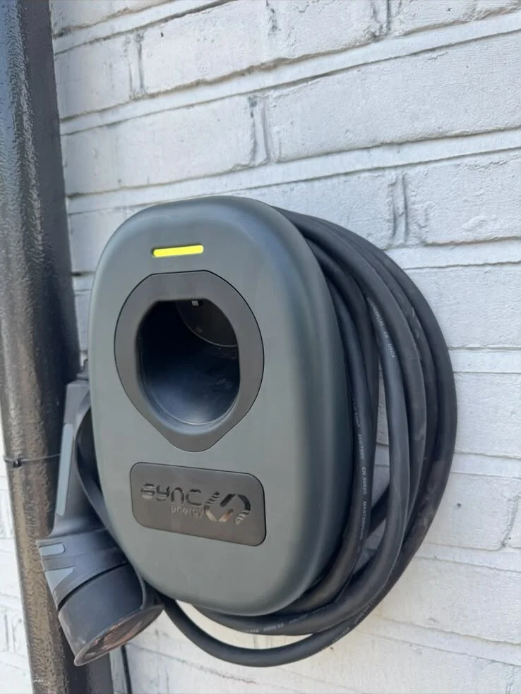Grey wall-mounted EV charger with its cable coiled round it